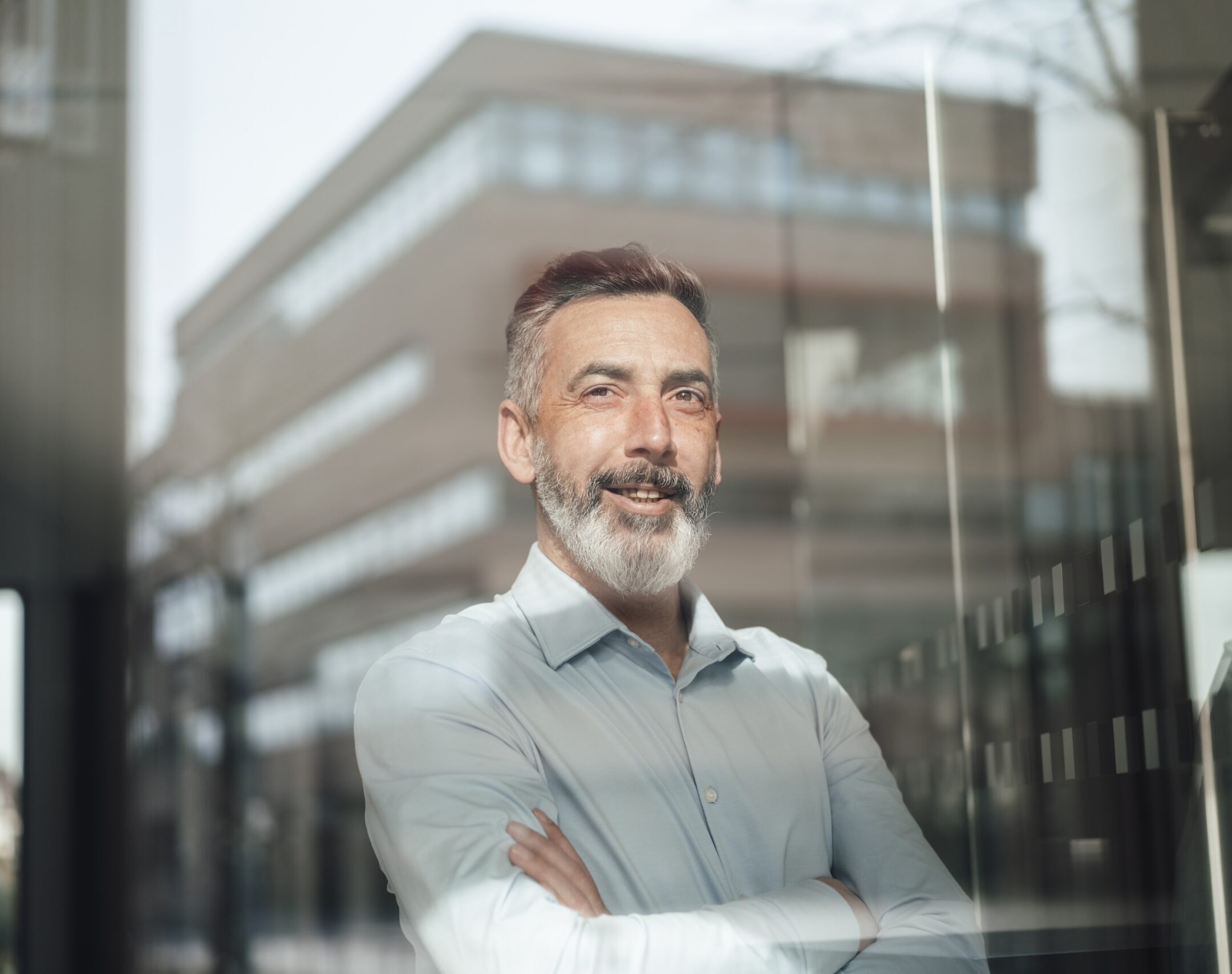 Smiling businessman standing with arms crossed seen through glass