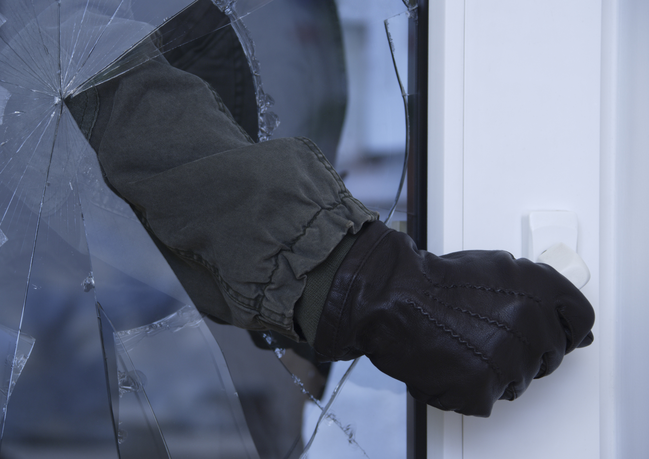 Inbreker grijpt door gebroken glas in deur